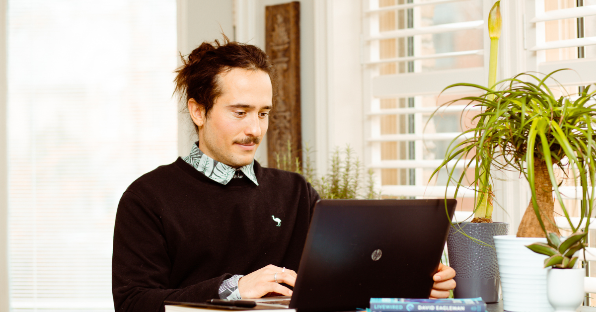 Digital marketer on his laptop sitting at a table with plants and books.