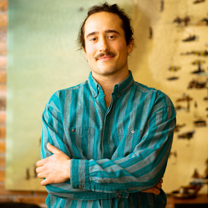 Digital marketer standing infront of a peice of art on a brick wall with his arms crossed.